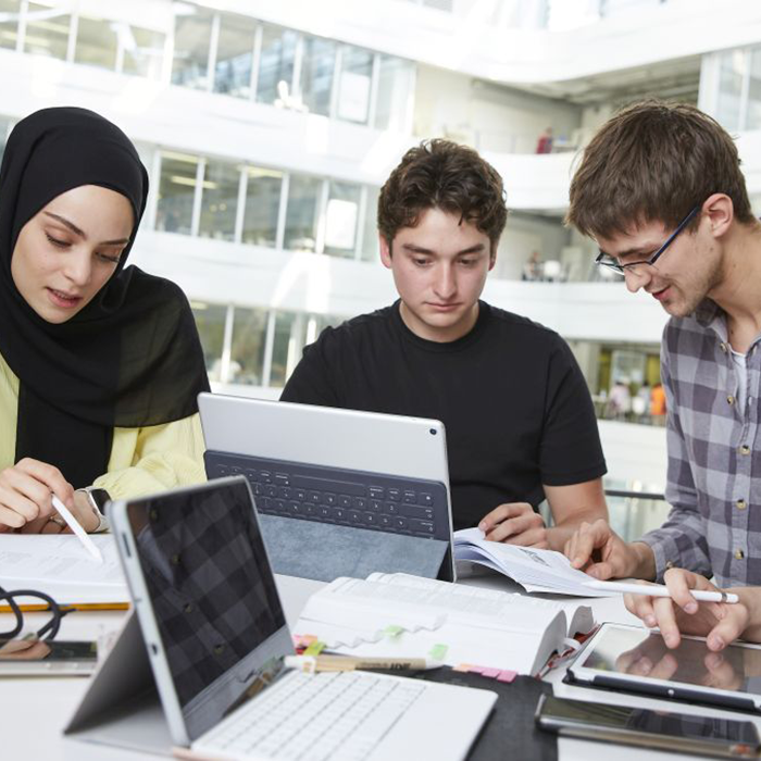 links eine Studentin und rechts von ihr zwei Studenten die gemeinsam Lernaufgaben lösen